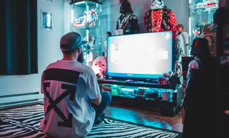 Back view of anonymous male sitting on floor near modern monitor and playing video game in room with comic stuff