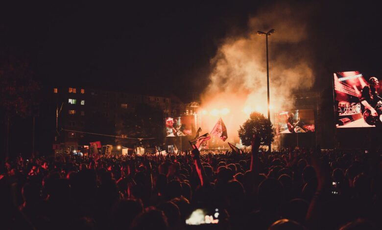 A dynamic live music concert with a large crowd, stage lights, and performer spotlight.
