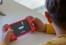 Child holding a pink handheld game console while a digital game loads on the screen.
