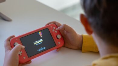 Child holding a pink handheld game console while a digital game loads on the screen.