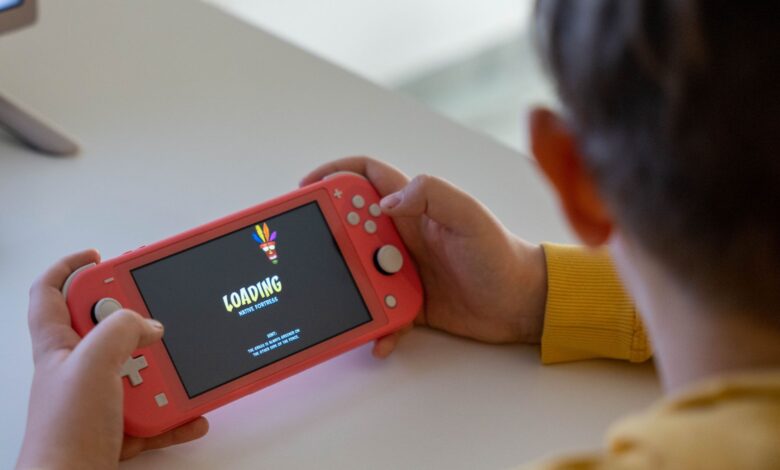 Child holding a pink handheld game console while a digital game loads on the screen.