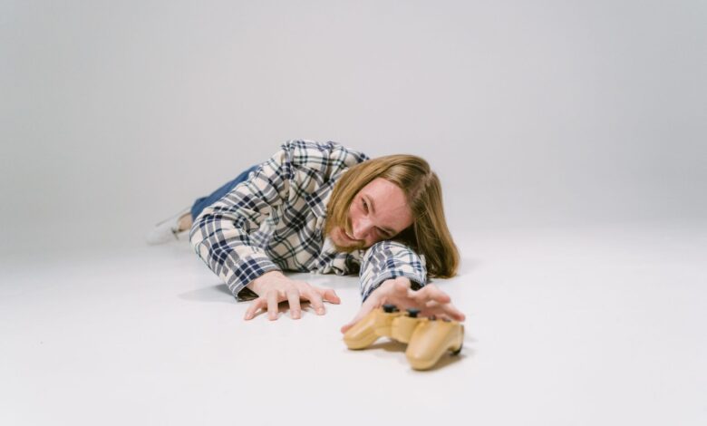 Young man in plaid shirt reaching for a controller on white studio floor.