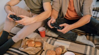 Two friends having fun playing video games with controllers and eating burgers indoors.