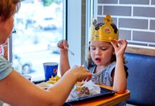 A child wearing a paper crown eats with mother at a fast food restaurant.