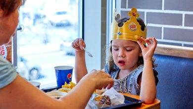 A child wearing a paper crown eats with mother at a fast food restaurant.