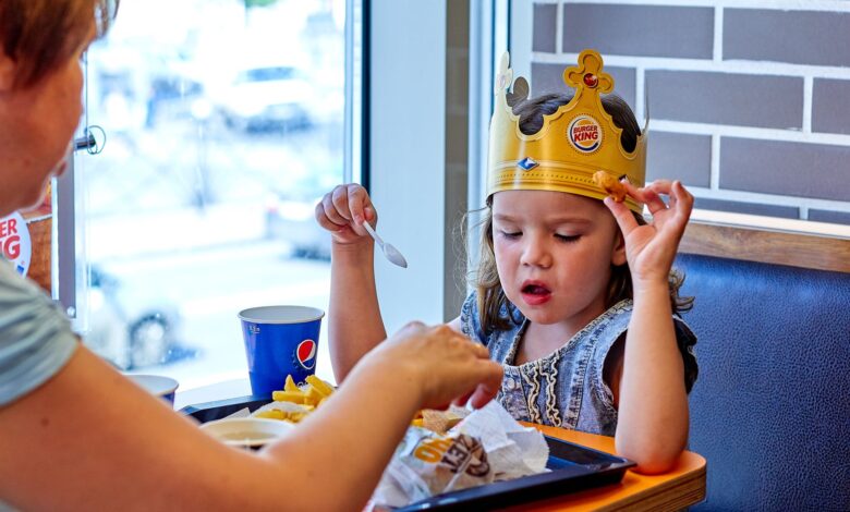 A child wearing a paper crown eats with mother at a fast food restaurant.