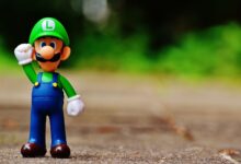 Close-up of a Luigi figurine from a videogame standing on outdoor pavement, showcasing fun and play.