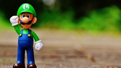 Close-up of a Luigi figurine from a videogame standing on outdoor pavement, showcasing fun and play.
