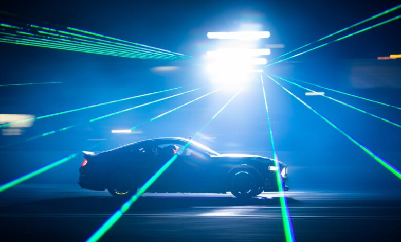 A car speeds through bright laser lights at night, creating dynamic light streaks.