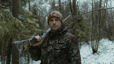 A man in camouflage holding a shotgun during winter hunting in the forest.