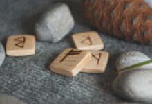 From above set of wooden runes and stones placed in knitted wool blanket near fir cone