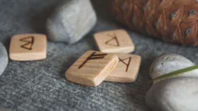 From above set of wooden runes and stones placed in knitted wool blanket near fir cone
