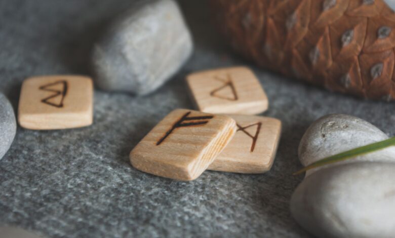 From above set of wooden runes and stones placed in knitted wool blanket near fir cone