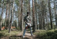 African American man operating a chainsaw in a forest setting.