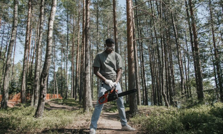African American man operating a chainsaw in a forest setting.