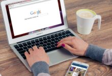 Hands typing on MacBook Air with Google search open, coffee nearby.