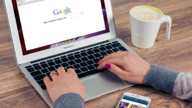 Hands typing on MacBook Air with Google search open, coffee nearby.