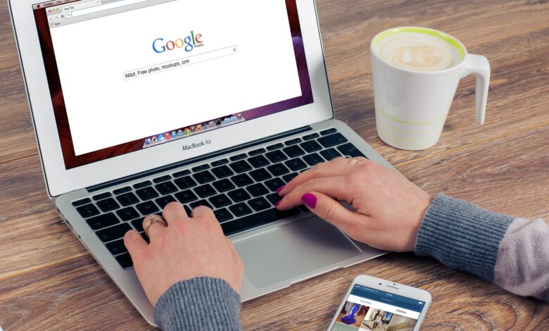 Hands typing on MacBook Air with Google search open, coffee nearby.