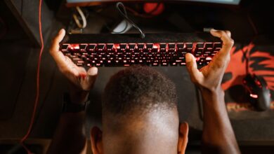 Gamer expresses frustration with video game by holding up keyboard. Overhead shot of gaming setup.
