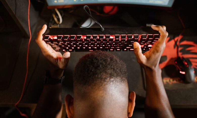 Gamer expresses frustration with video game by holding up keyboard. Overhead shot of gaming setup.