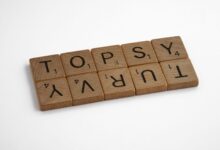 Close-up of wooden Scrabble tiles arranged to spell 'topsy turvy' on a white background.