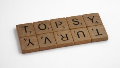 Close-up of wooden Scrabble tiles arranged to spell 'topsy turvy' on a white background.