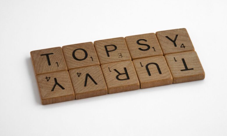 Close-up of wooden Scrabble tiles arranged to spell 'topsy turvy' on a white background.