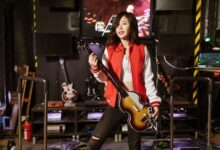 Woman playing Guitar Hero with guitar controller in a gaming room, enjoying the arcade experience.