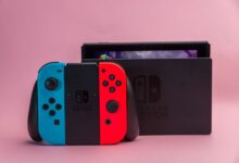 Close-up of Nintendo Switch console with red and blue Joy-Con controllers on pink background.