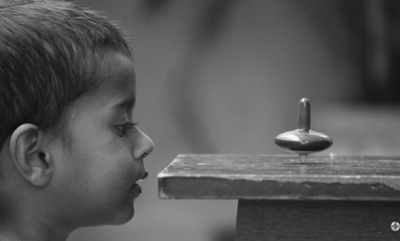 A curious child closely observes a spinning top with fascination.