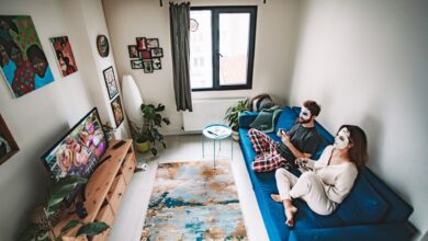 A couple playing video games on a couch with face masks, enjoying leisure time in a cozy living room.