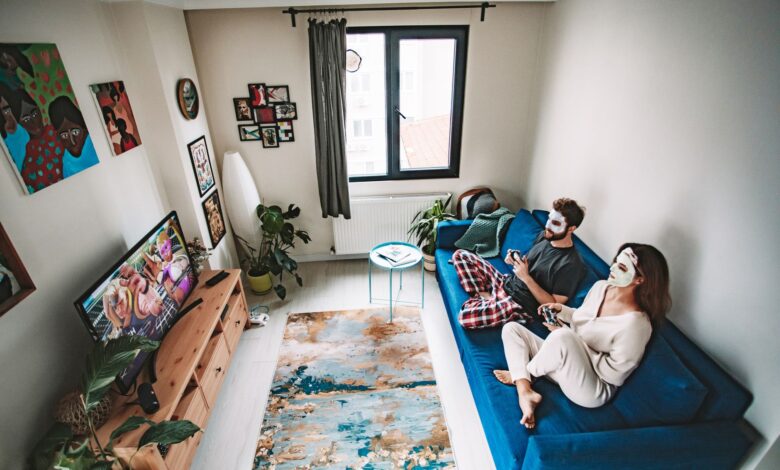 A couple playing video games on a couch with face masks, enjoying leisure time in a cozy living room.